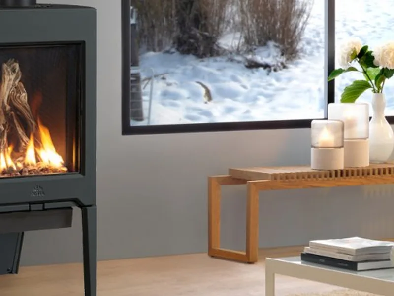 A Jøtul gas stove burning beside a window with snow outside
