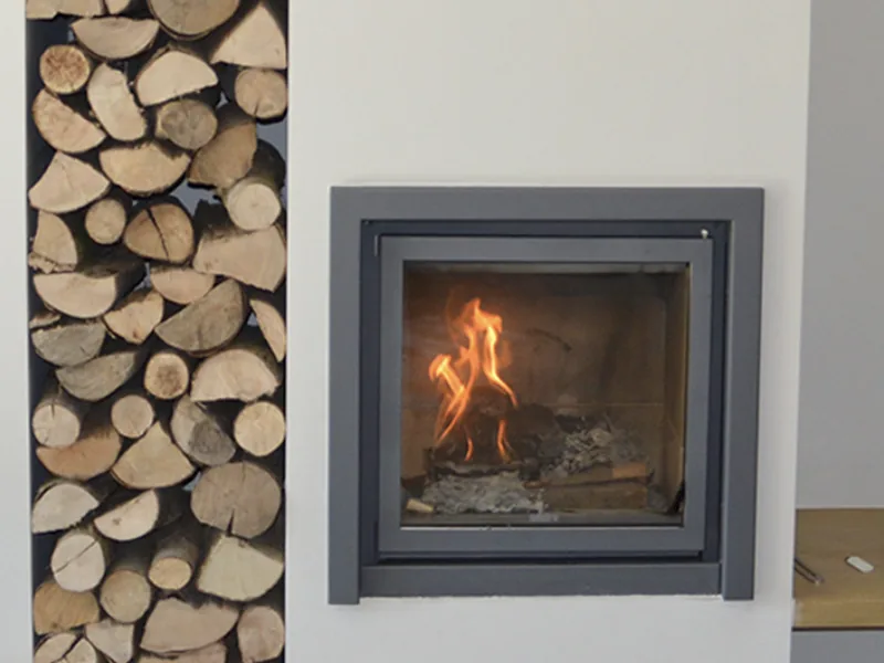 A Stûv wood fireplace burning beside a full log store