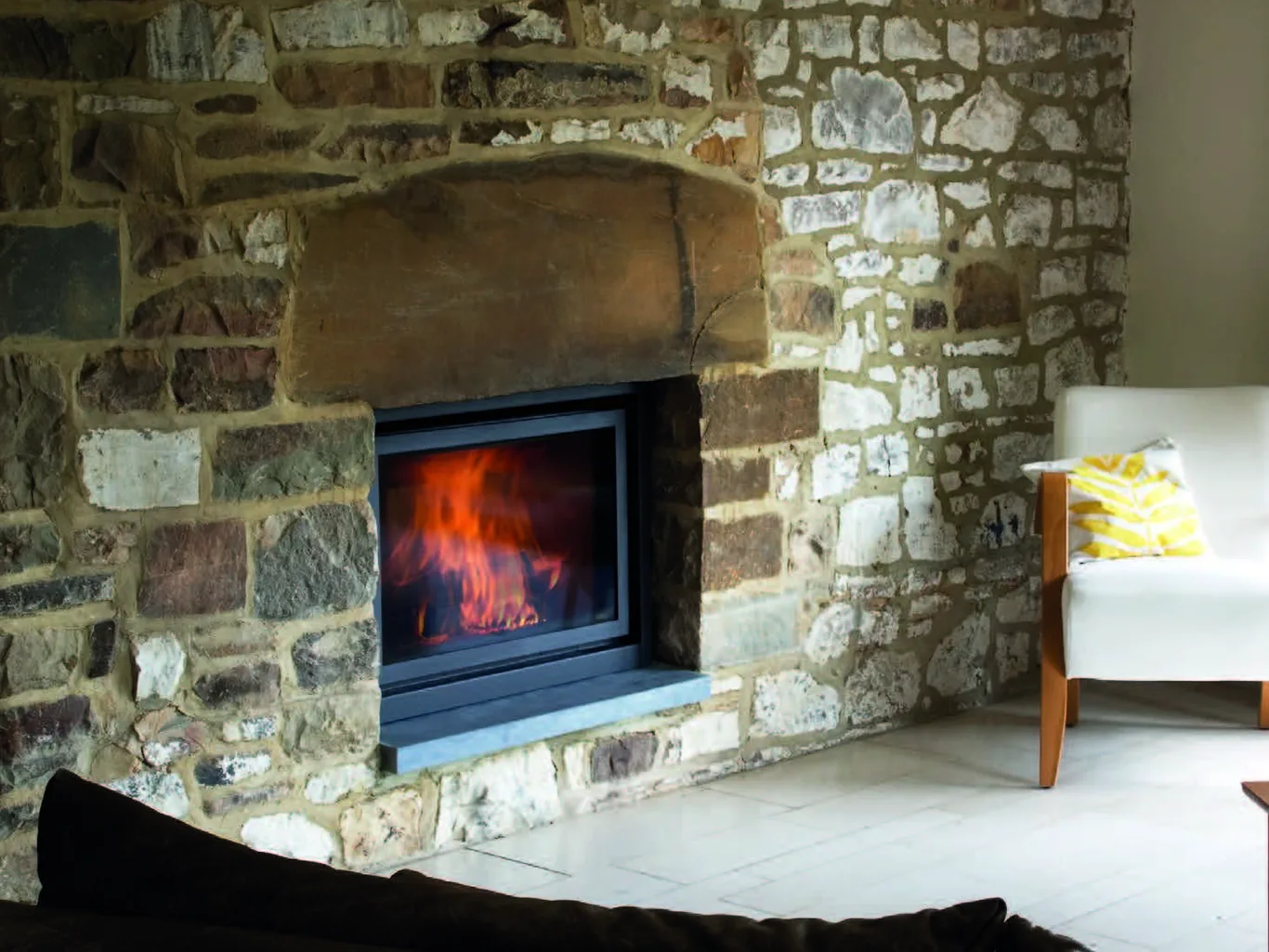 A Stûv wood insert burning in a rustic stone fireplace
