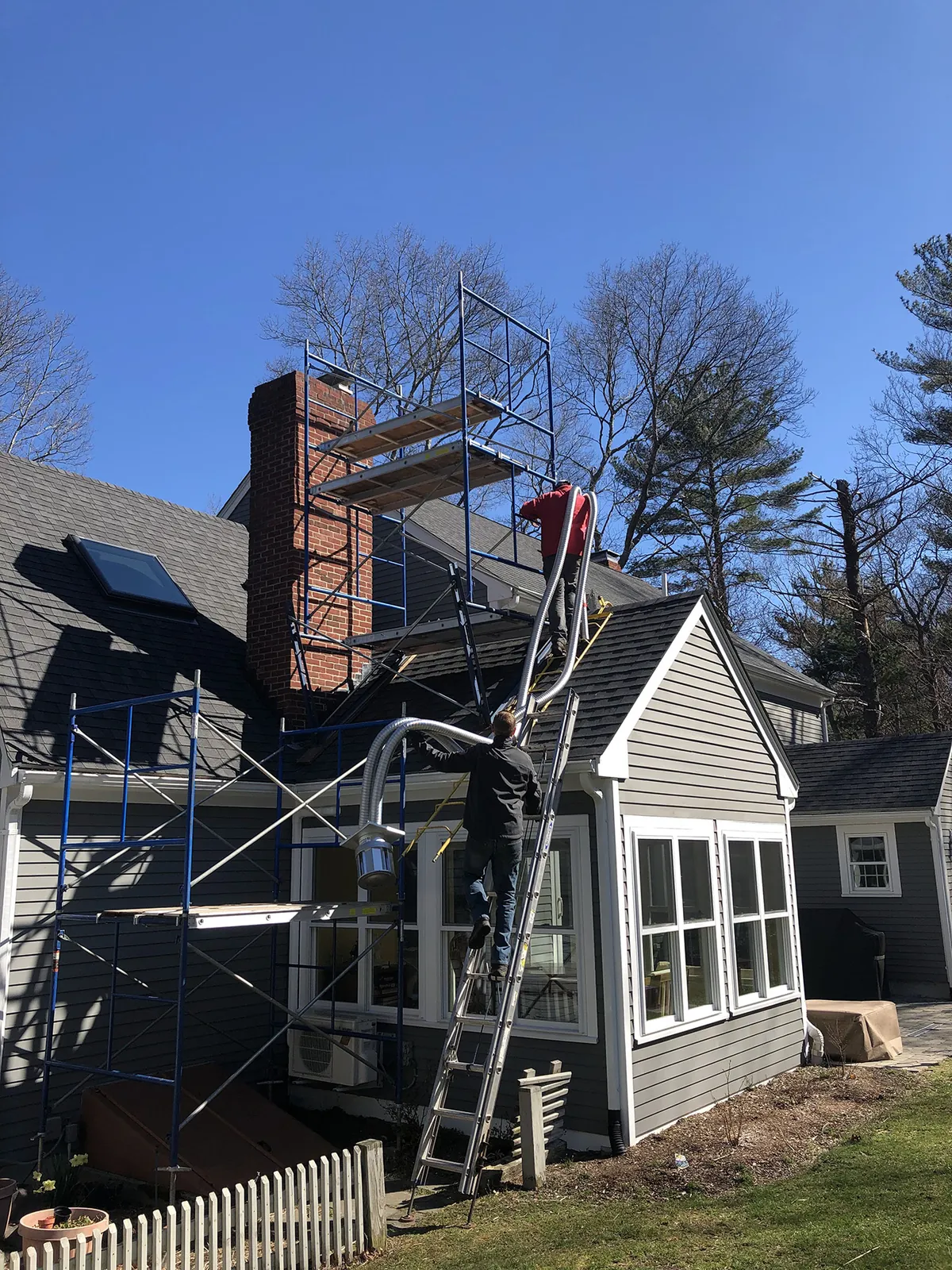 Masonry chimney rebuild in progress on a shingled house, scaffolding in place
