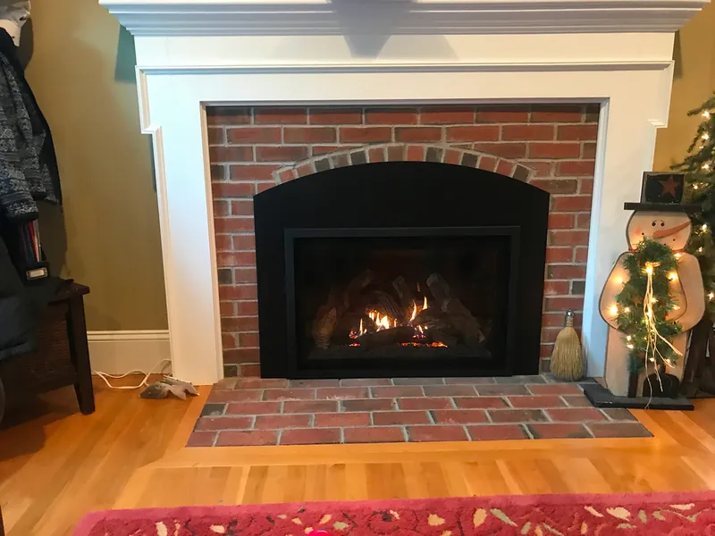 A gas insert burning in a brick fireplace with a white mantel