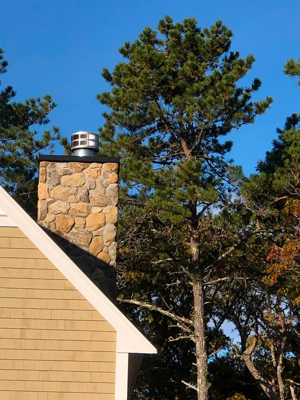 A fieldstone chimney against pine trees